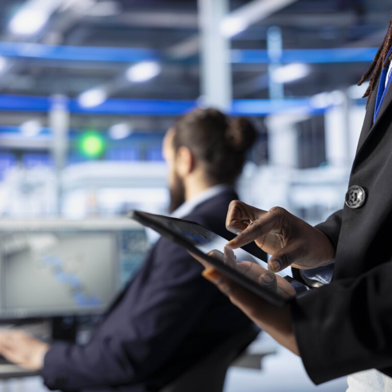 Woman on a tablet stands in front on a man working at a computer.
