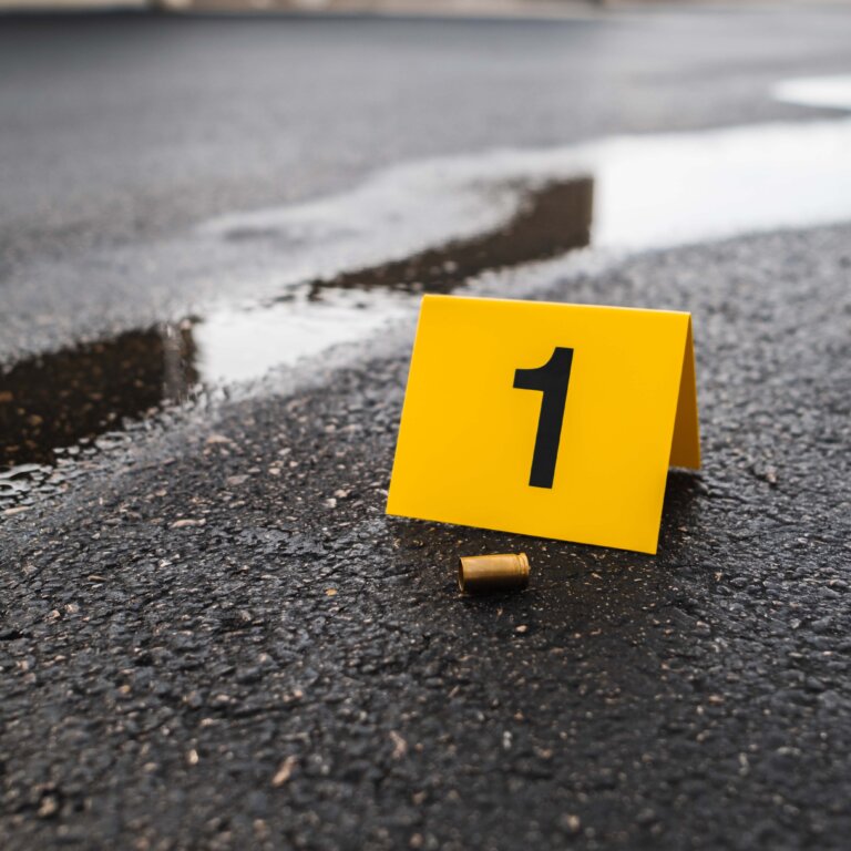 One yellow crime scene evidence marker on the street next to a bullet casing.