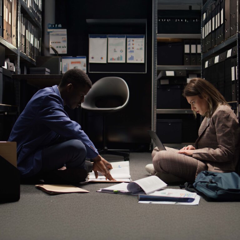  Two detectives sit on the floor looking through files for a case.
