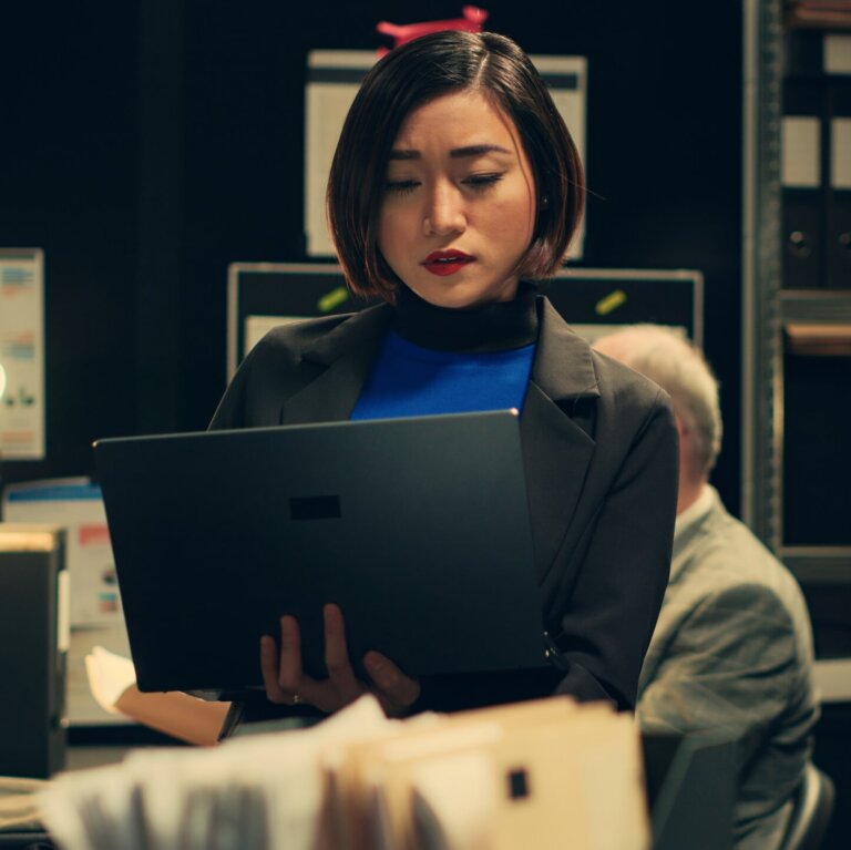  Private investigator searching for old case folders in archive room, comparing witness statements and interviews across multiple investigations.