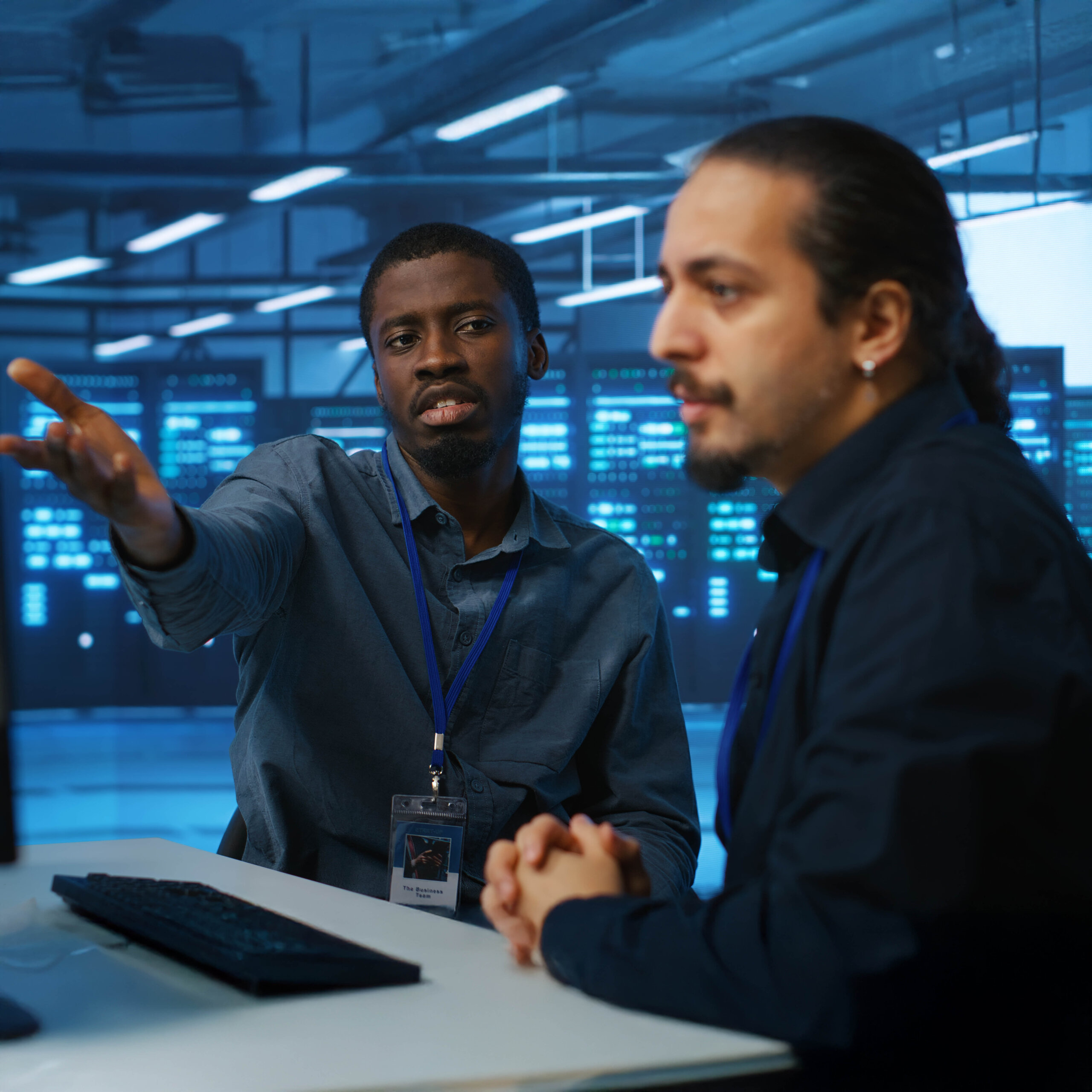 Two men sitting at a desk in a security center pointing and discussing what is on the screen.
