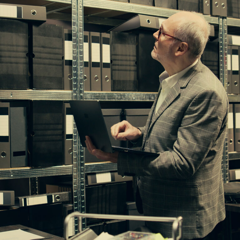  Investigator reviewing archived paper case files while using a laptop, highlighting the challenges of an outdated RMS and the need for modern records management software.